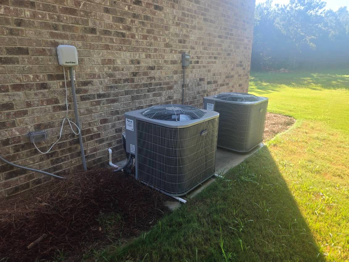 Two outdoor condenser units installed beside a brick home
